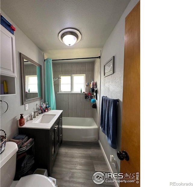 bathroom featuring toilet, wood finished floors, shower / bath combination with curtain, vanity, and a textured ceiling