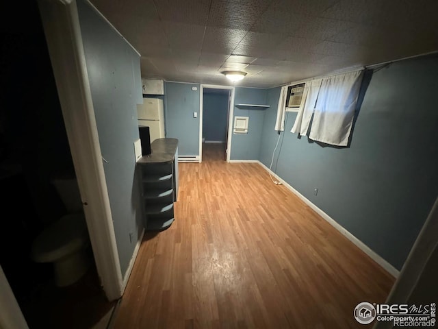 corridor with a baseboard heating unit, light wood-style flooring, and baseboards