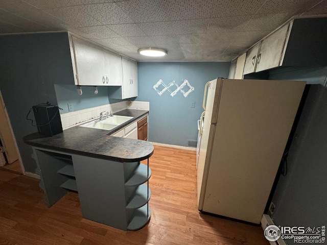 kitchen with open shelves, dark countertops, light wood-style floors, freestanding refrigerator, and a sink