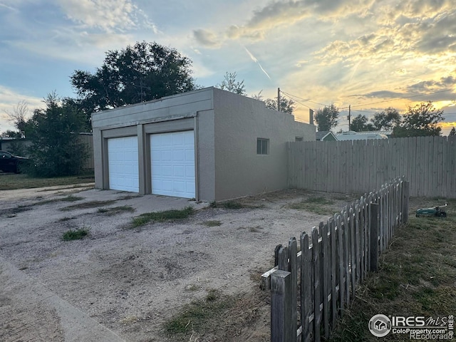 garage at dusk with a garage and fence