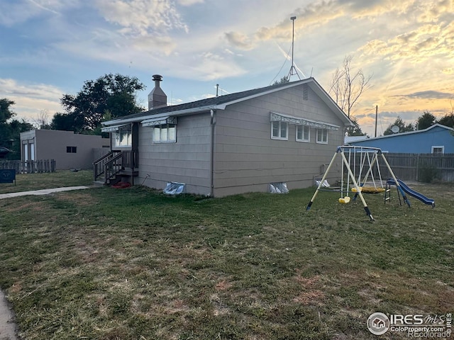 exterior space with a chimney, a lawn, a playground, and fence