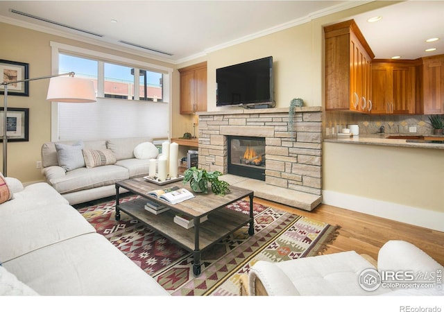 living room with light wood-type flooring, crown molding, and a fireplace