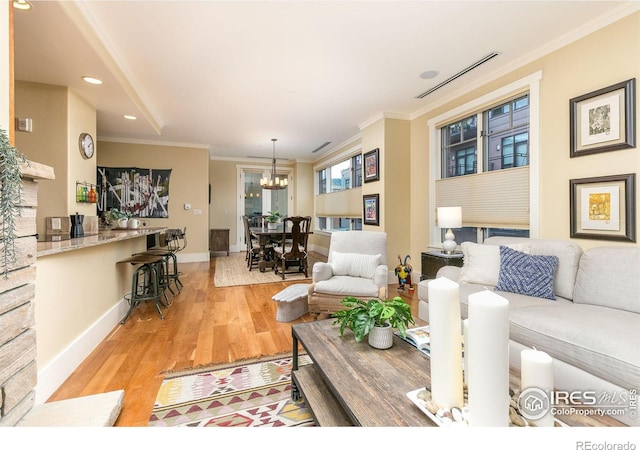 living room featuring light hardwood / wood-style flooring, ornamental molding, and an inviting chandelier