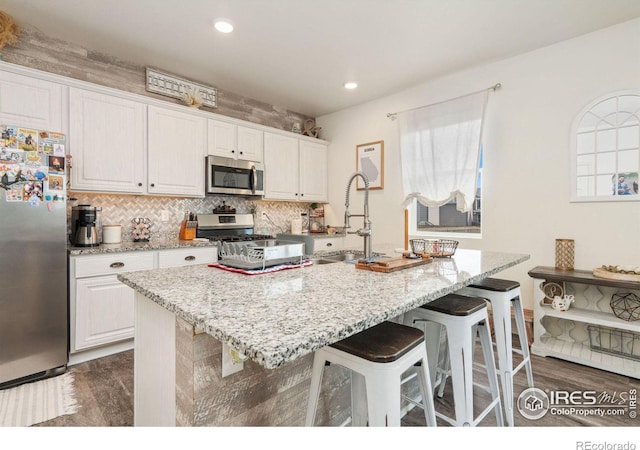 kitchen featuring a kitchen breakfast bar, stainless steel appliances, sink, a center island with sink, and white cabinets