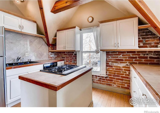 kitchen featuring sink, white cabinets, vaulted ceiling with beams, light hardwood / wood-style floors, and tile counters