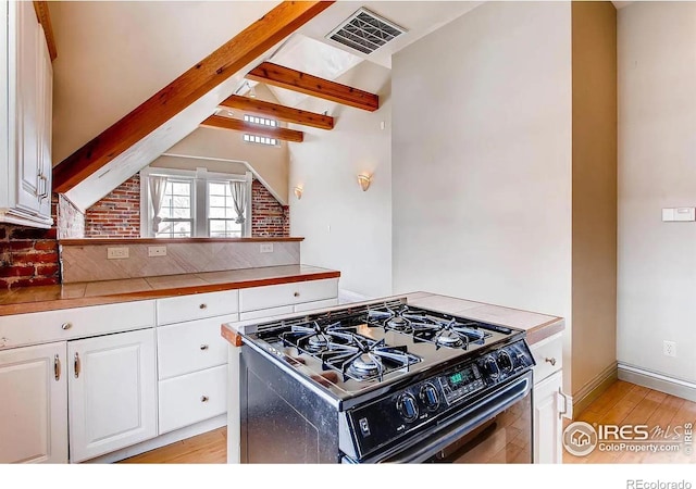 kitchen with brick wall, tile countertops, light hardwood / wood-style flooring, white cabinets, and black gas stove