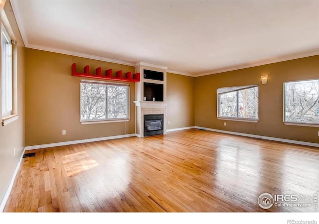 unfurnished living room with a wealth of natural light, ornamental molding, and light wood-type flooring