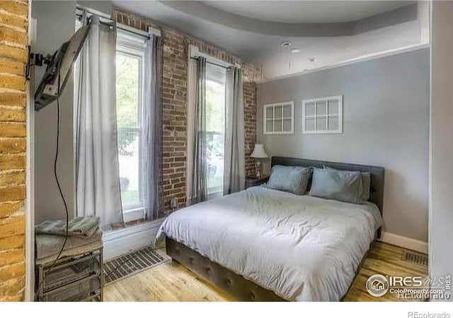 bedroom with hardwood / wood-style floors and brick wall