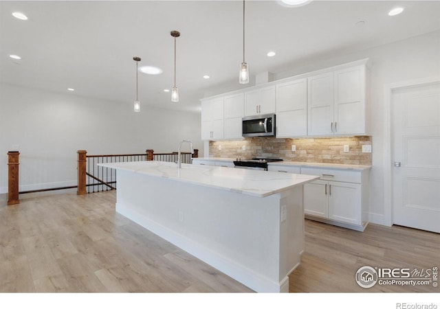 kitchen featuring light stone countertops, pendant lighting, stainless steel appliances, a center island with sink, and white cabinetry