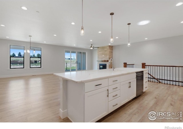 kitchen with decorative light fixtures, a fireplace, a kitchen island with sink, and white cabinets