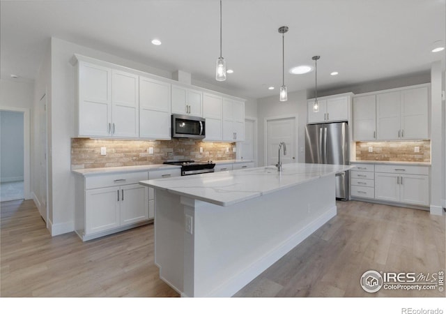 kitchen featuring stainless steel appliances, white cabinetry, a kitchen island with sink, and backsplash