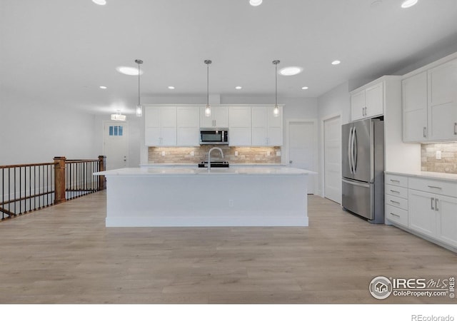 kitchen with hanging light fixtures, stainless steel appliances, an island with sink, white cabinets, and sink