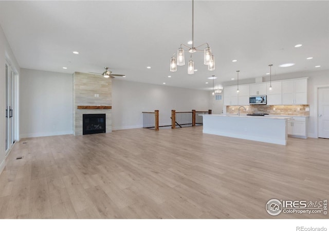 unfurnished living room featuring ceiling fan, a tiled fireplace, light hardwood / wood-style floors, and sink