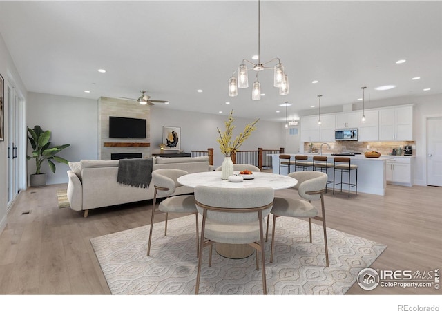 dining area with a large fireplace, ceiling fan, and light hardwood / wood-style floors