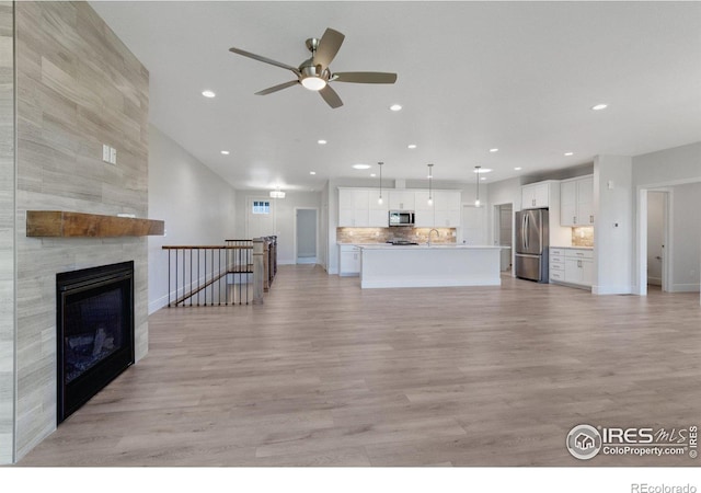 unfurnished living room featuring sink, ceiling fan, light wood-type flooring, and a fireplace