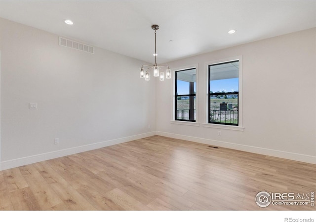 spare room with light hardwood / wood-style floors and a chandelier