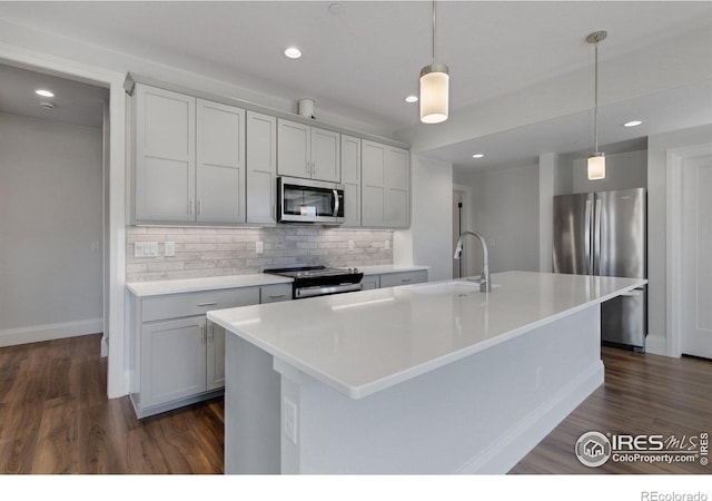 kitchen with decorative light fixtures, a center island with sink, tasteful backsplash, appliances with stainless steel finishes, and sink