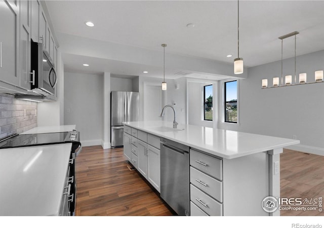 kitchen with appliances with stainless steel finishes, an island with sink, decorative light fixtures, and sink