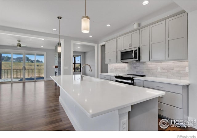 kitchen featuring stainless steel appliances, decorative light fixtures, tasteful backsplash, and a kitchen island with sink