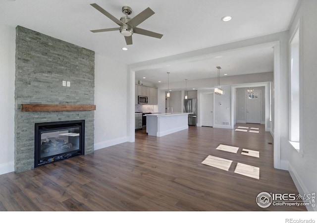 unfurnished living room featuring ceiling fan with notable chandelier, sink, dark hardwood / wood-style flooring, and a stone fireplace