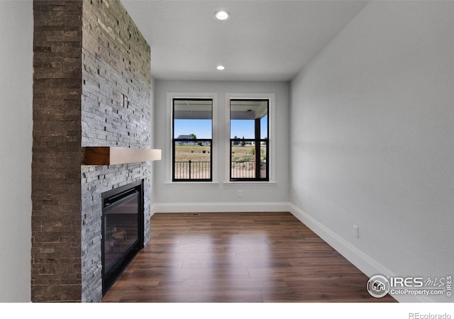 unfurnished living room with dark hardwood / wood-style flooring and a stone fireplace