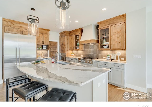 kitchen with pendant lighting, custom exhaust hood, an island with sink, sink, and white cabinetry