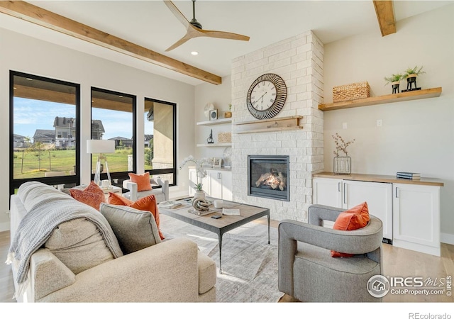 living room featuring beamed ceiling, a brick fireplace, ceiling fan, and light hardwood / wood-style flooring