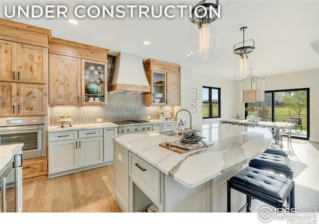 kitchen featuring stainless steel appliances, a sink, decorative backsplash, a center island with sink, and custom range hood