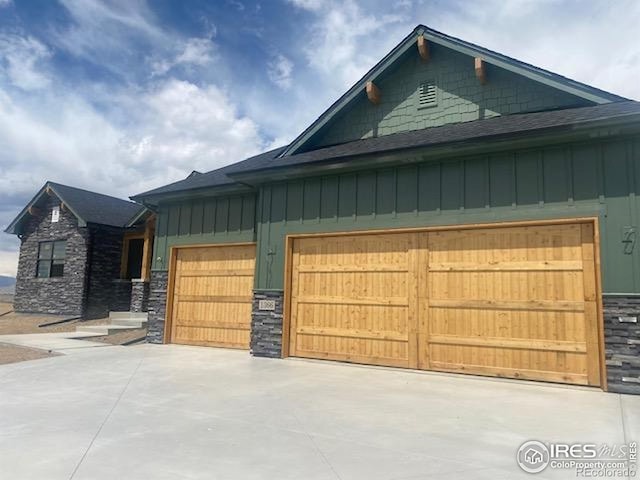 exterior space featuring an attached garage, driveway, stone siding, and board and batten siding