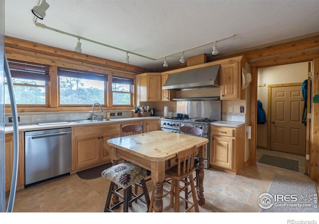 kitchen featuring stainless steel appliances, track lighting, sink, light tile patterned flooring, and wall chimney exhaust hood