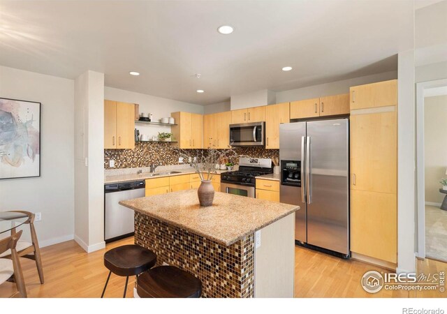 kitchen with stainless steel appliances, sink, decorative backsplash, light wood-type flooring, and a center island