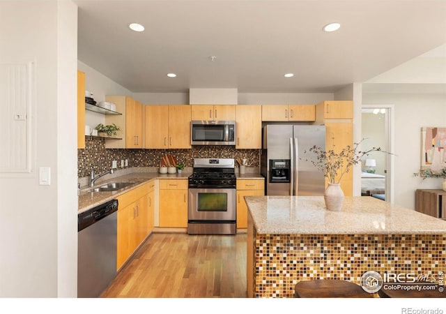 kitchen featuring light wood-type flooring, light stone countertops, appliances with stainless steel finishes, decorative backsplash, and sink