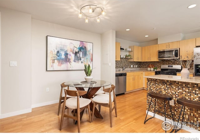 kitchen with appliances with stainless steel finishes, light hardwood / wood-style flooring, tasteful backsplash, sink, and light brown cabinetry