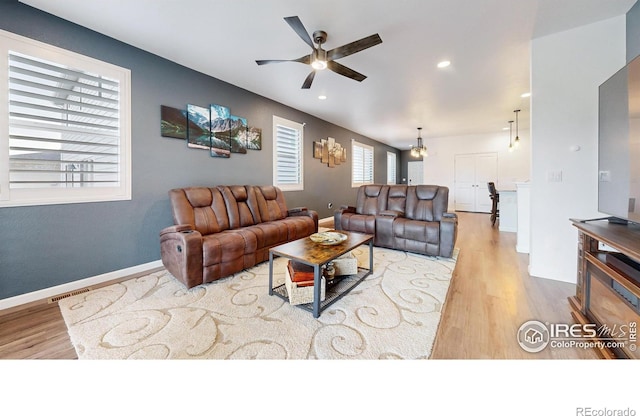 living room with ceiling fan with notable chandelier and light hardwood / wood-style flooring