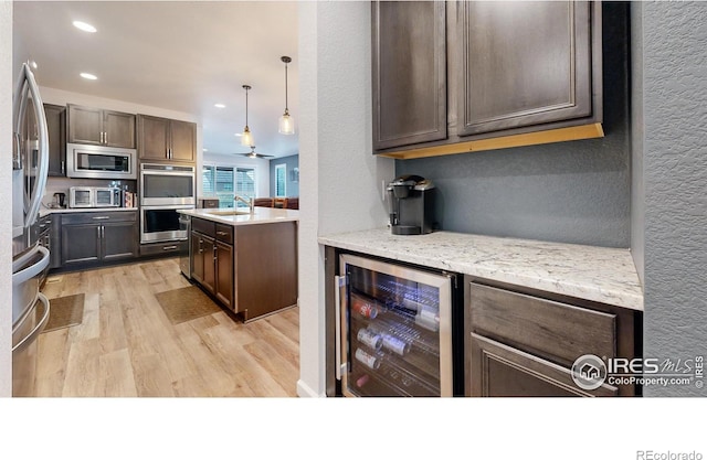 kitchen with wine cooler, appliances with stainless steel finishes, decorative light fixtures, light hardwood / wood-style floors, and dark brown cabinetry