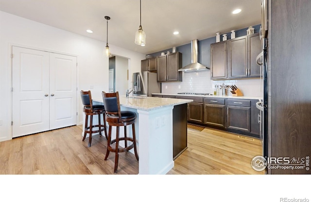 kitchen with decorative backsplash, a kitchen breakfast bar, stainless steel appliances, wall chimney range hood, and an island with sink