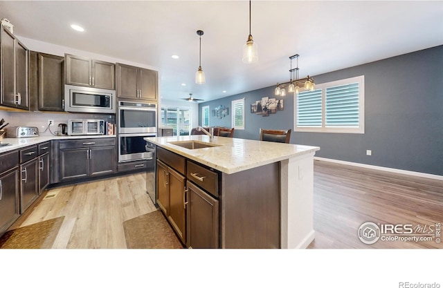 kitchen with appliances with stainless steel finishes, light wood-type flooring, hanging light fixtures, and an island with sink