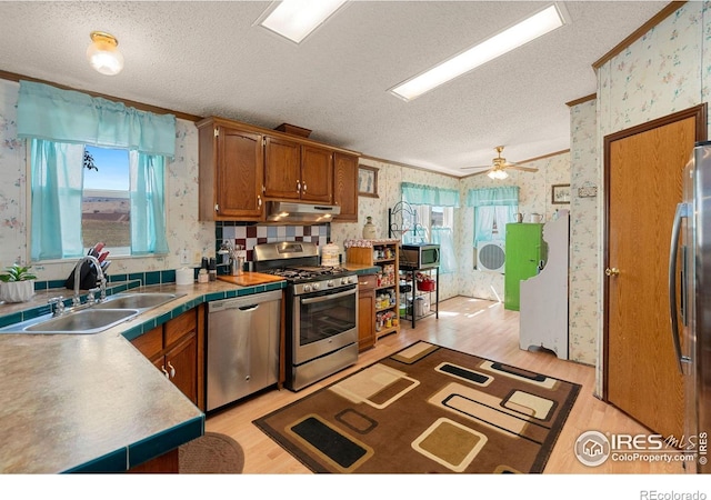 kitchen featuring a textured ceiling, light hardwood / wood-style flooring, appliances with stainless steel finishes, ceiling fan, and sink