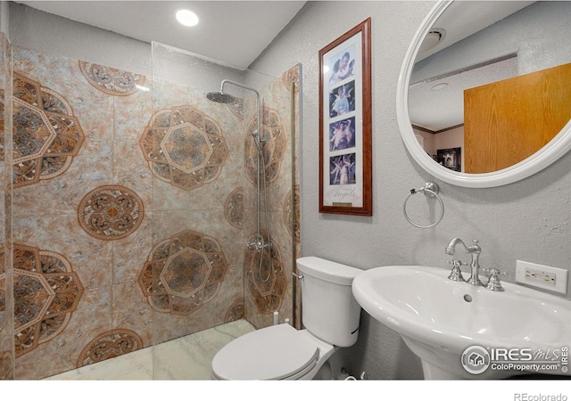 bathroom with sink, tiled shower, and toilet