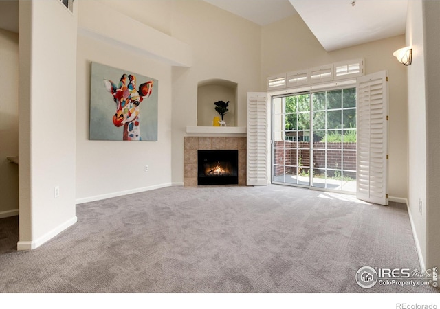 unfurnished living room with a tile fireplace, carpet floors, and a high ceiling