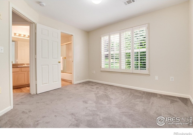 unfurnished bedroom with ensuite bathroom, sink, and light colored carpet