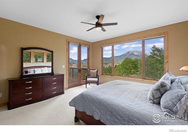 carpeted bedroom with multiple windows, access to exterior, ceiling fan, and a mountain view