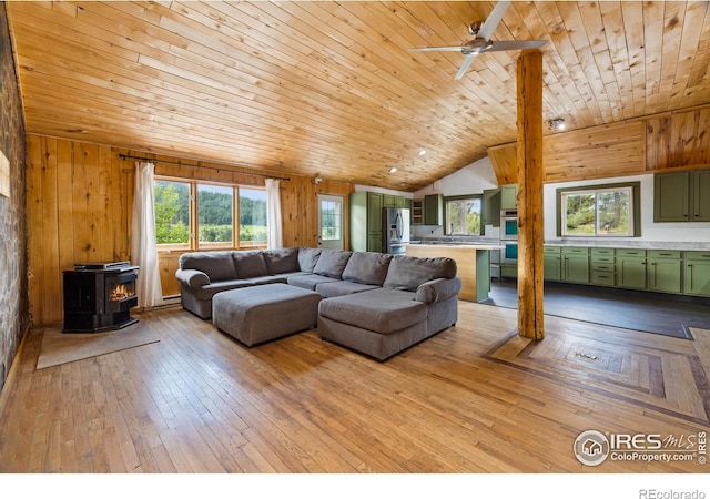 living room featuring a wood stove, wood ceiling, lofted ceiling, wood walls, and ceiling fan