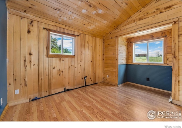 spare room featuring light wood-type flooring, wooden walls, and vaulted ceiling