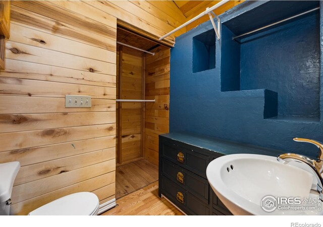 bathroom featuring sink, wooden walls, wood-type flooring, and toilet