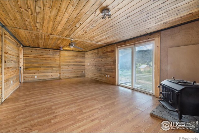 interior space featuring a wood stove, light hardwood / wood-style flooring, wooden ceiling, and wooden walls