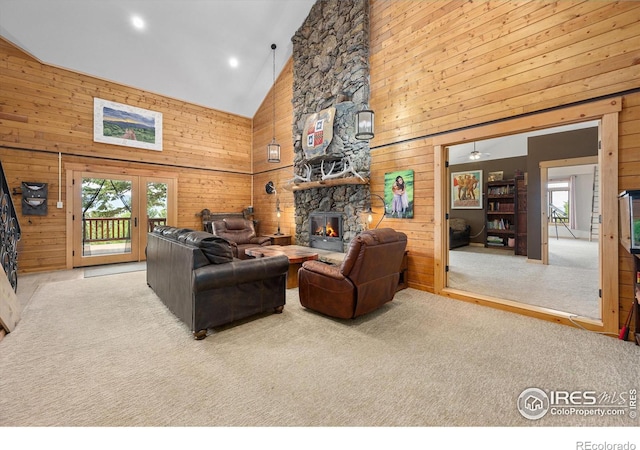 living room with wooden walls, a stone fireplace, high vaulted ceiling, and carpet