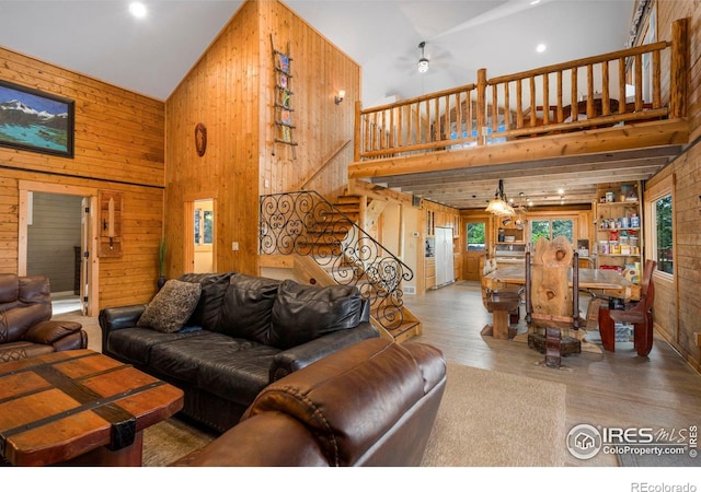 living room with ceiling fan, wooden walls, light hardwood / wood-style floors, and high vaulted ceiling