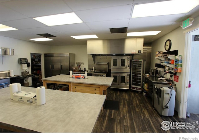 kitchen with beverage cooler, dark wood finished floors, a kitchen island, light countertops, and a paneled ceiling