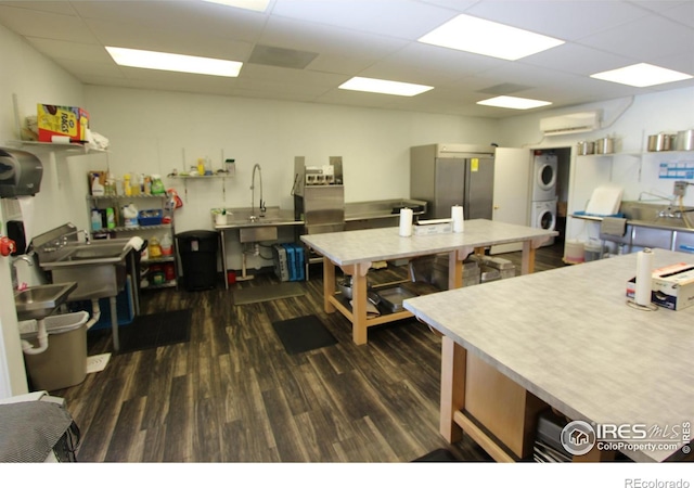 kitchen with a drop ceiling, dark wood-style floors, stacked washer / drying machine, freestanding refrigerator, and an AC wall unit